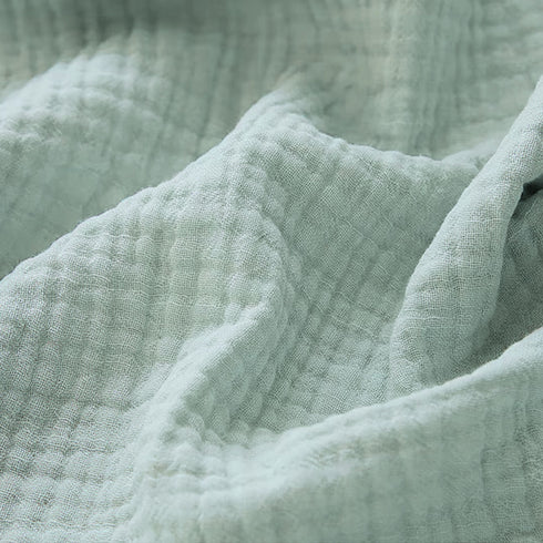 Couverture pour bébé en gaze de coton, dans un élégant coloris bleu vert, mettant en valeur ses finitions délicates visibles en détail sur l’image.