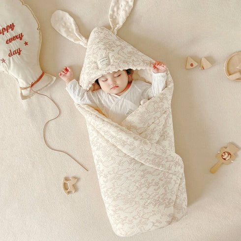 un bébé dans une couverture à capuche bébé ou couverture d'emmaillotage motif de faune, avec petits lapins et écureuil écru et marron clair avec oreille de lapin