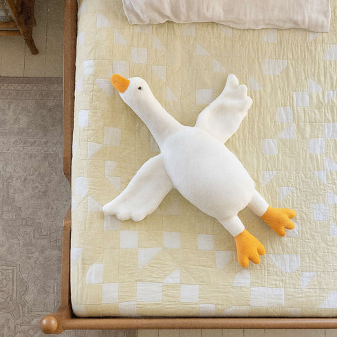 Peluche canard blanche Bellemoon posée sur un lit aux motifs géométriques jaunes