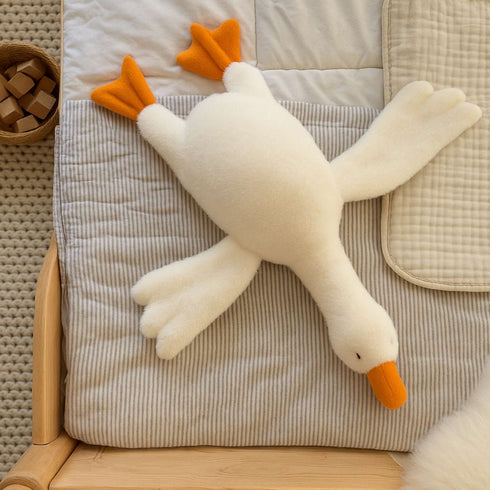 Peluche canard blanche avec ailes ouvertes sur un coussin rayé dans une chambre d’enfant