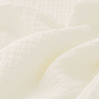 Couverture pour bébé en gaze de coton, dans un coloris blanc pur, révélant ses finitions raffinées grâce aux détails visibles en zoom.