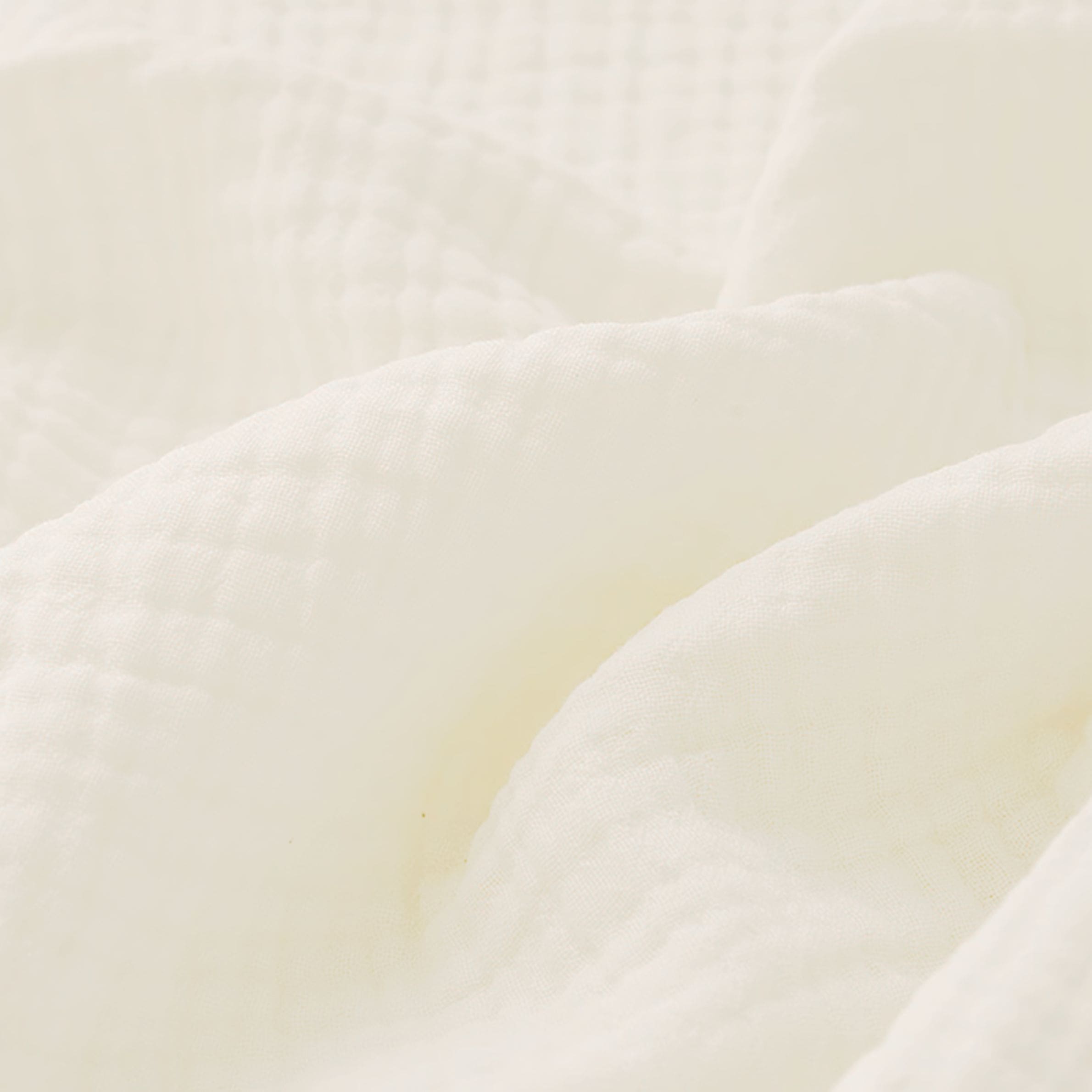 Couverture pour bébé en gaze de coton, dans un coloris blanc pur, révélant ses finitions raffinées grâce aux détails visibles en zoom.