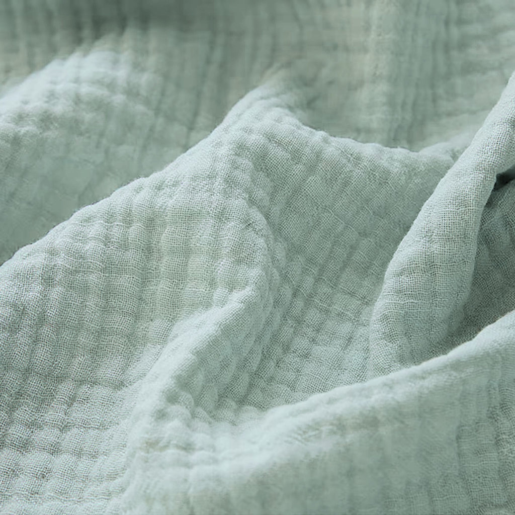Couverture pour bébé en gaze de coton, dans un élégant coloris bleu vert, mettant en valeur ses finitions délicates visibles en détail sur l’image.