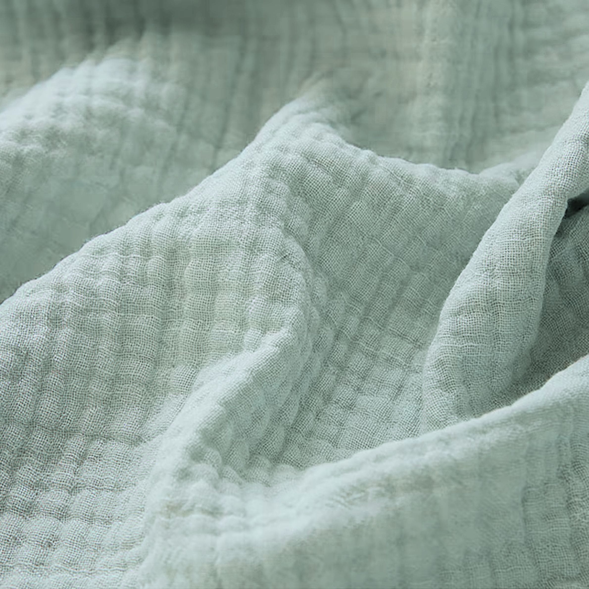 Couverture pour bébé en gaze de coton, dans un élégant coloris bleu vert, mettant en valeur ses finitions délicates visibles en détail sur l’image.