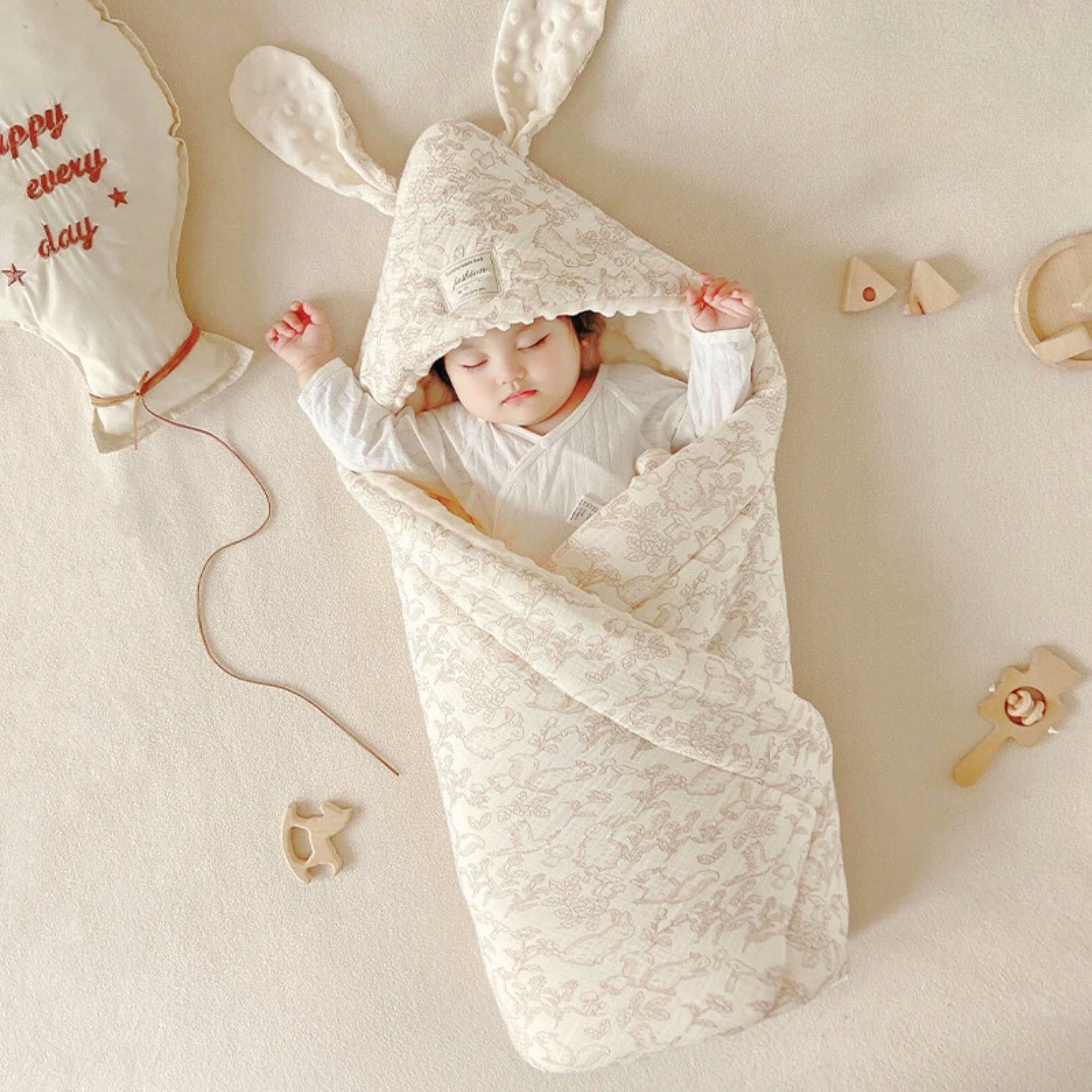 un bébé dans une couverture à capuche bébé ou couverture d'emmaillotage motif de faune, avec petits lapins et écureuil  écru et marron clair avec oreille de lapin